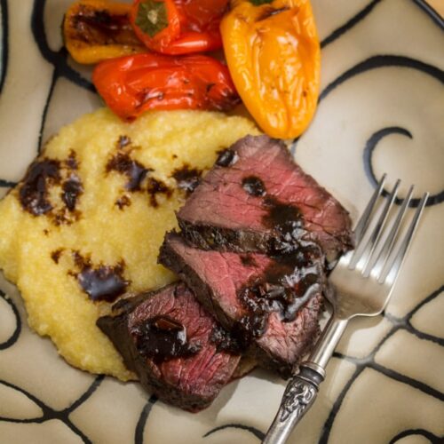 Plate of Balsamic Red Wine Marinated London Broil with polenta and peppers.