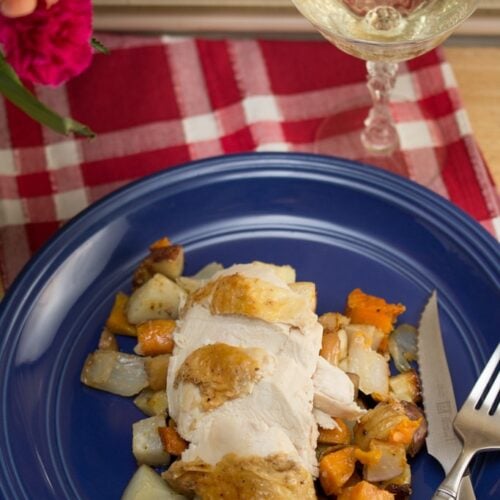 A plate of roasted chicken and veggies with a glass of wine and flowers.