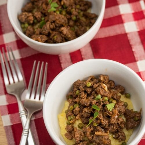 Two bowls of ground beef with peas and rosemary over grits.