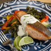 A plate of salmon with roasted veggies and a yogurt sauce.