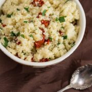 Bowl of couscous with sun-dried tomatoes and parsley.