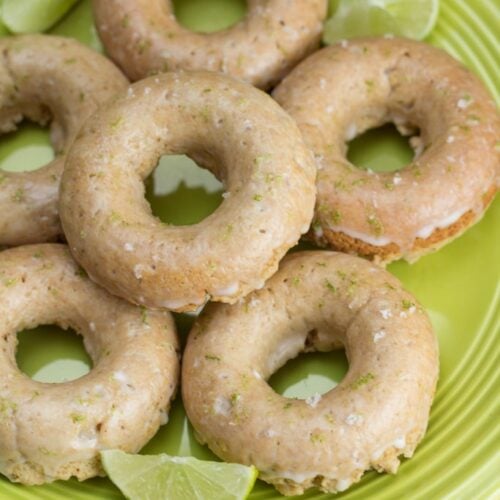 Overhead view of a plate of donuts with lime wedges on a green plate.