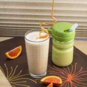 Two smoothies - one in a glass and one in a child's cup with oranges alongside.