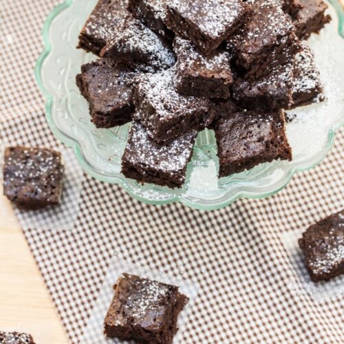 Overhead view of brownies on a cake stand, dusted with powdered sugar.