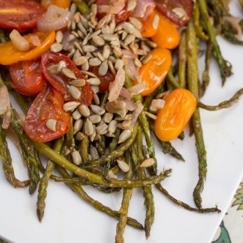Overhead view of roasted asparagus and tomatoes with toasted sunflower seeds.