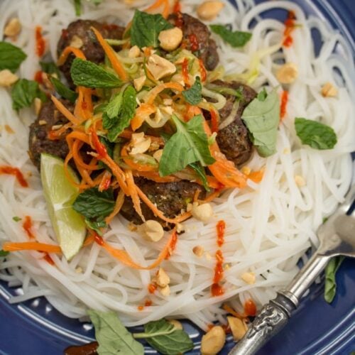 Plate of rice noodles topped with meatballs, fresh herbs, and lime.