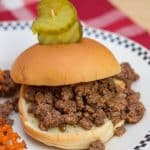 Sloppy Joe sandwich on a plate with waffle fries and pickles.