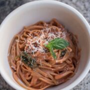 A bowl of creamy tomato pasta with basil on top.