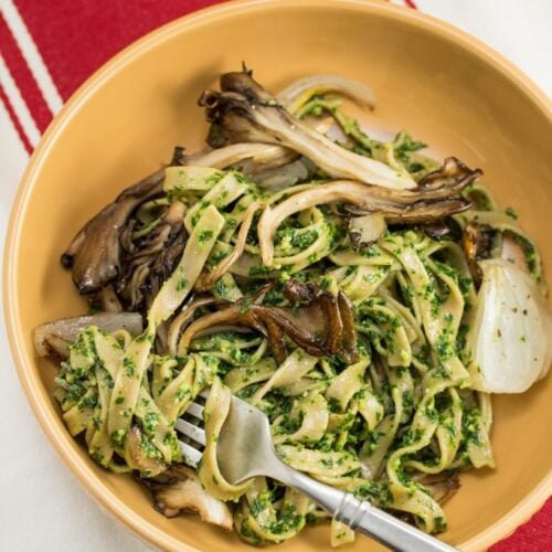 Bowl of Farmer Fettuccine with Kale Pesto + Roasted Maitake Mushrooms with a fork.