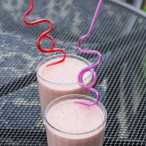 Smoothies with swirly straws sitting on an outdoor table.