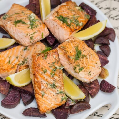 Salmon and purple sweet potatoes on a platter with dill and lemon wedges.