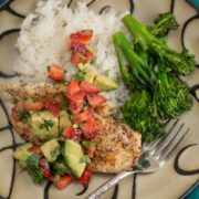 A plate of chicken topped with strawberry and avocado with broccolini.