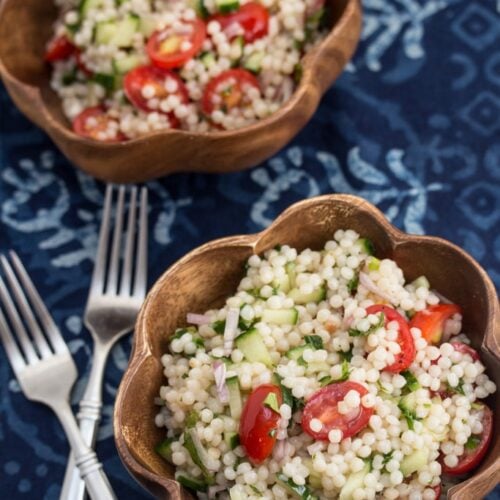 Overhead view of Israeli couscous tabbouleh in 2 bowls with forks alongside.