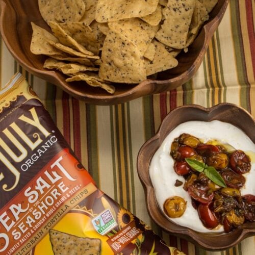 Bowl of tortilla chips and whipped goat cheese dip topped with balsamic tomatoes and basil.
