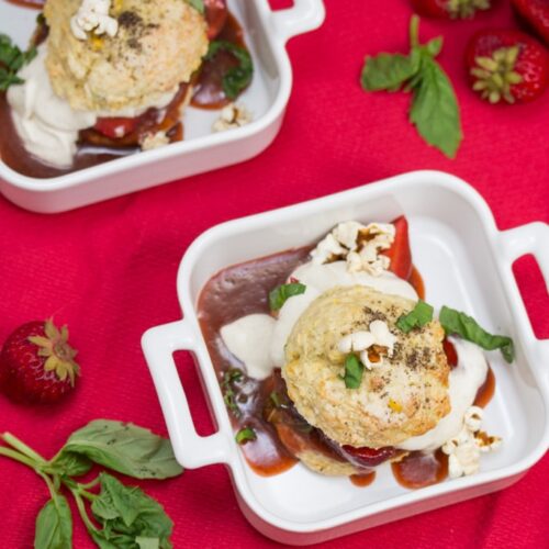 Overhead view of 2 bowls of strawberry shortcake with fresh basil, whipped cream, and popcorn.