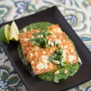 Broiled tofu slices on a plate with cilantro pesto and lime wedges.