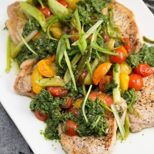 A plate of pork medallions topped with veggies and green sauce.