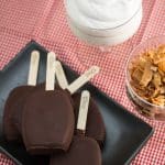 Ice cream bars on a platter with toasted coconut chips and whipped cream.