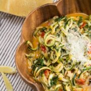 Bowl of zucchini noodles with lemon, tomatoes, and greens topped with Parmesan cheese.