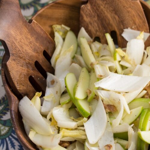 Endive and walnut salad with apples in a serving bowl with serving tools.