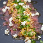 Platter of thinly sliced raw tuna with peach and corn topping, popcorn, and micro greens.