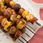 Platter of grilled and skewered shrimp, sausage, potatoes, and corn.