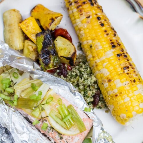 Plate of salmon cooked in a foil packet with grilled corn and mixed vegetables alongside.