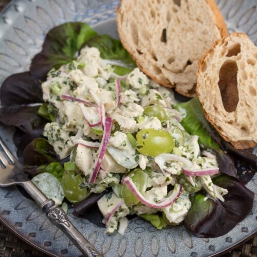 A plate of chicken salad with grapes and sliced bread.
