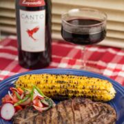 Plate of grilled steak and corn with salad and red wine.