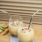 Side view of 2 pineapple rum cocktails with lime wedges on a cutting board alongside.