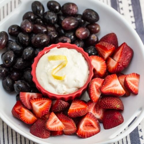 A bowl of fruit with a ramekin of lemon cream fruit dip in the center.