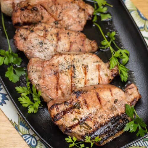 Platter of grilled pork chops garnished with parsley sprigs.