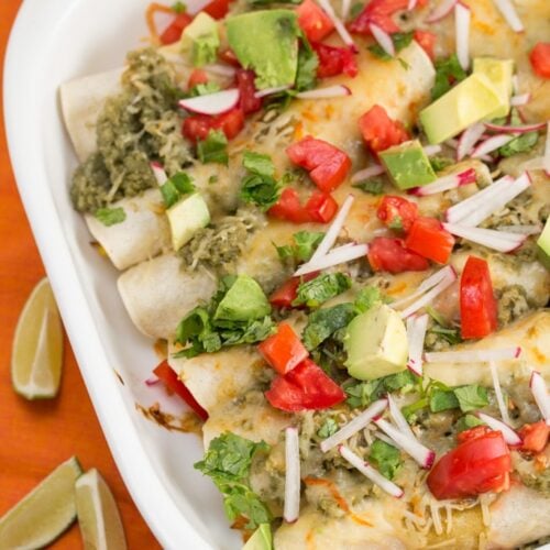 Baking dish of pork enchiladas with colorful toppings.