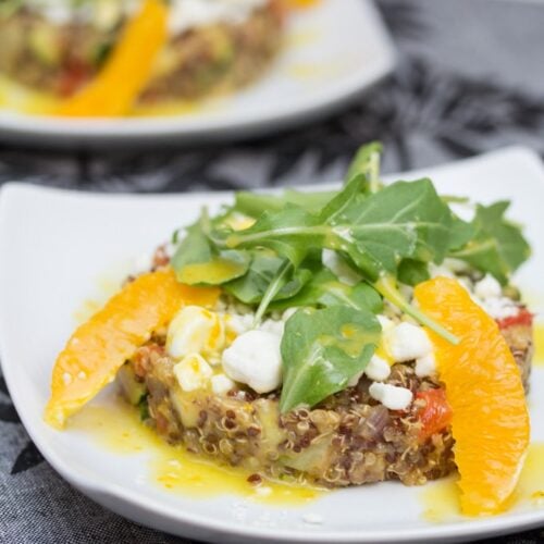 Close-up view of quinoa salad topped with goat cheese, oranges, and arugula.