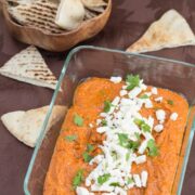 Overhead view of muhammara dip topped with feta and pita bread alongside.