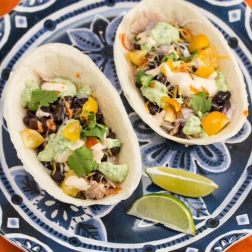 A plate of chipotle pork tacos with lime wedges.