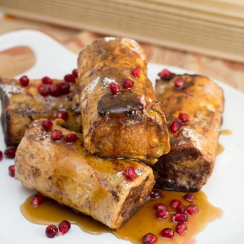 A platter of pain perdu topped with maple syrup and pomegranate arils.