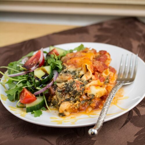 A plate of spinach lasagna with salad.