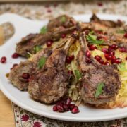 A plate of lamb chops over spaghetti squash garnished with pomegranate arils.