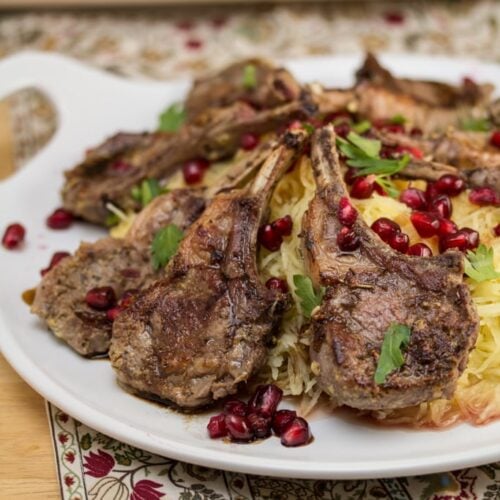 A plate of lamb chops over spaghetti squash garnished with pomegranate arils.