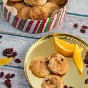 A tin of cranberry orange snickerdoodles with orange slices alongside.