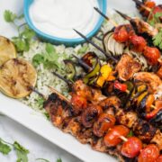 A platter of grilled chicken fajita skewers over cauliflower rice with dipping sauce.