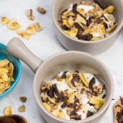 Bowls of Greek yogurt parfaits topped with banana chips, chocolate chunks, and walnuts.