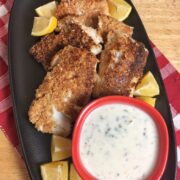 A platter of cod with lemon wedges and a bowl of tartar sauce.