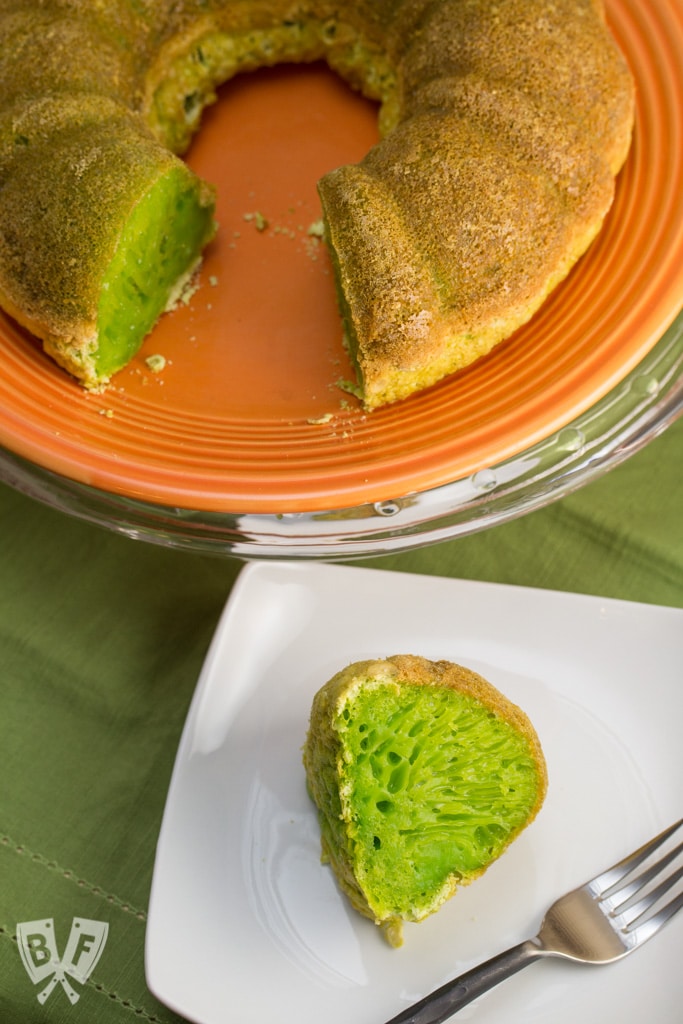 A green bundt cake on a plate with a slice placed on a smaller plate with a vibrant green filling.