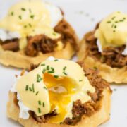 A platter with 3 waffles topped with pulled pork, poached eggs, hollandaise sauce, and chives.