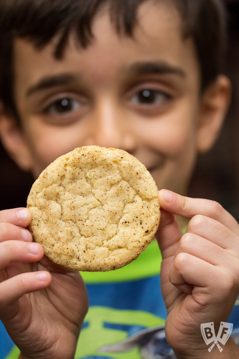 Close-up view of a child holding a Chai-Spiced Snicekerdoodle Cookie