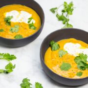 Overhead view of 2 bowls of curried pumpkin soup with cilantro leaves, sour cream, and chili oil garnish.