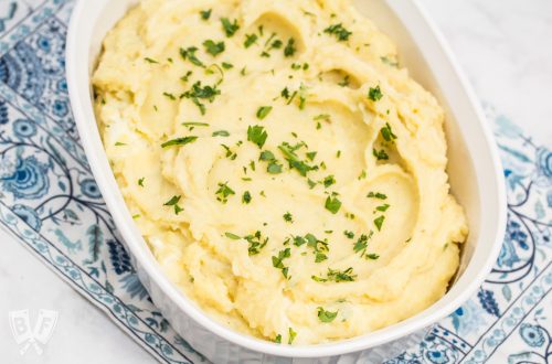 Overhead shot of an oval casserole dish full of creamy mashed potatoes sprinkled with chopped parsley.