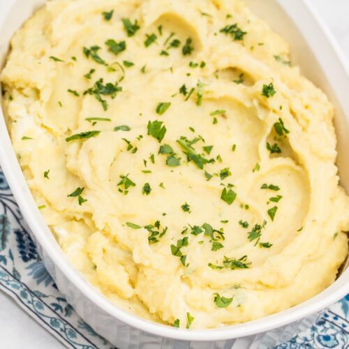 Overhead shot of an oval casserole dish full of creamy mashed potatoes sprinkled with chopped parsley.